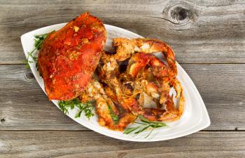 High angled view of freshly cooked crab with spicy sauce and herbs on white serving plate. Rustic wood underneath dish. 