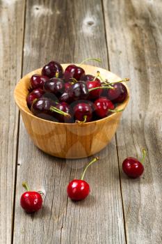 Close up image of freshly picked whole black cherries in bowl on rustic wooden table. Layout in vertical format.