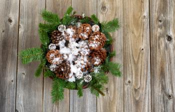 Christmas basket filled with pine tree branches, cones and snow on rustic wooden boards. 
