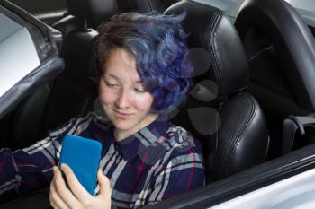Teenage girl, cell phone in hand, looking at text while in driver seat of car. Focus on her face. Mixed Asian and Caucasian girl. 