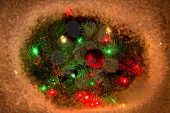 Red Christmas ornament and lights hanging from real fir tree branches with snow border. Night time Christmas season concept.