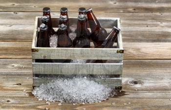 Vintage crate filled with bottled beer and crushed ice on rustic wooden boards. 