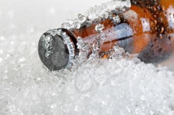 Close up view of a beer bottle neck covered with ice and condensation. Layout in horizontal format. Focus on bottle cap with shallow depth of field.