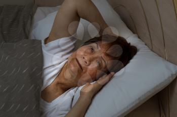 Close up of senior woman, eyes open looking upward, trying to fall asleep. Insomnia concept. 