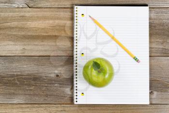 Top view of green apple, notepad and pencil on rustic wood.