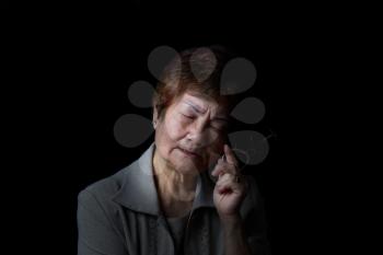 Senior woman displaying pain while holding reading glass on black background.