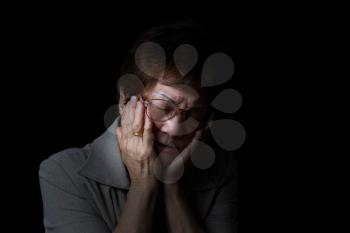 Senior woman holding her face with both hands while displaying pain on black background.