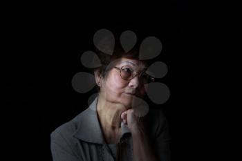 Senior woman resting her chin with one hand while displaying loneliness on black background. Depression concept. 