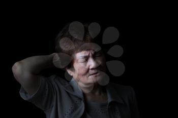 Senior woman touching the back of her head while displaying pain on black background.