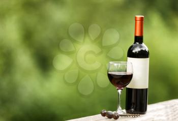 Glass of red wine with full bottle and corkscrew on rustic wood outdoors. Selective focus on front of wine glass with shallow depth of field on horizontal layout. 