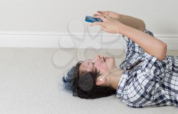 Teen girl looking at cell phone while lying on her back listening to music at home. 
