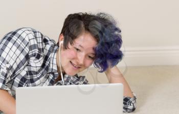 Smiling teen girl looking at computer while listening to music at home. 