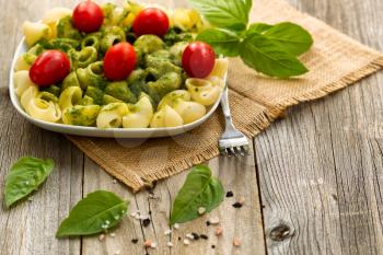 Basil pesto with shell shaped pasta and cherry tomatoes. Selective focus on front part of plate.