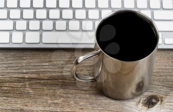 Selective focus on lip of coffee mug with partial keyboard in background. Layout in horizontal format on rustic wood. 