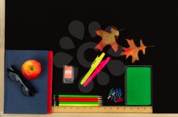 School supplies plus autumn leaves on blackboard. Back to school concept for fall season.