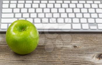 Selective focus on ripe green apple with partial keyboard in background. Layout in horizontal format on rustic wood. 