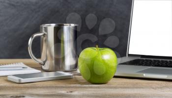 Selective focus of a fresh green apple on school desk with technology. Layout in horizontal format with copy space. 