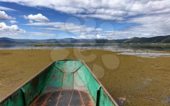 Empty small fishing boat on wetland with mountains and sky in background.