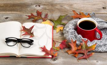 Coffee, autumn leaves, book, reading glasses and grey scarf on rustic wood.