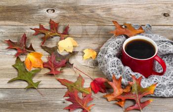 Close up view of a hot cup of black coffee, autumn leaves and grey scarf on rustic wood.