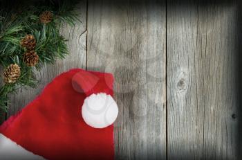 
Santa cap and evergreen branch on rustic wood with vignette border. Christmas concept. 
