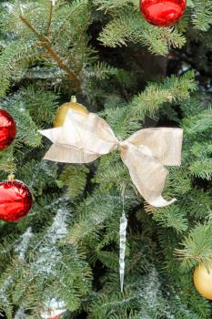 Close up of gold colored ribbon, in center, hanging in Christmas tree with several other ornaments covered in snow. Selective focus on golden ribbon in filled framed 