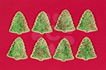 Christmas tree shaped cookies organized on red background.