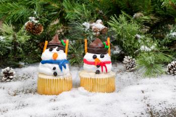 Cupcake snowmen with light snow and evergreen background. 