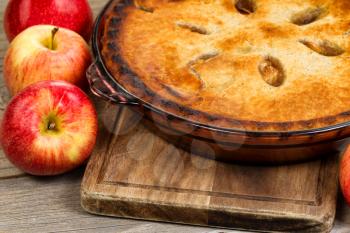 Close up of freshly baked apple with whole apples and wooden server board on rustic wood.