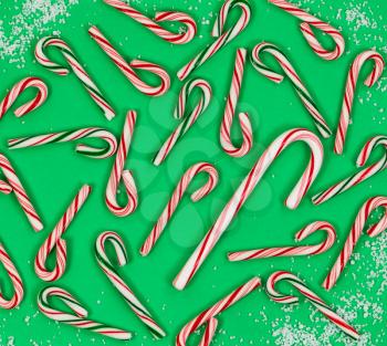 High angle shot of various candy canes and light snow on green background. Holiday concept with filled frame layout. 