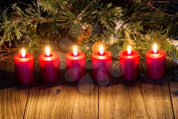 Burning red candles with snow covered evergreens and rustic wood. 