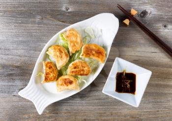 High angled view of Chinese dumpling with sauce in bowl with chopsticks on rustic wood. 