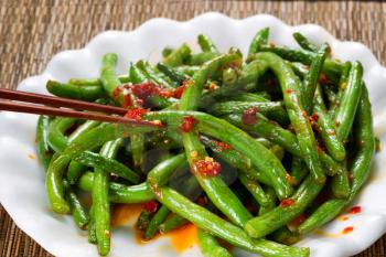 Close up view of spicy green beans with chopsticks in use. Selective focus on single bean being held by chopsticks. 