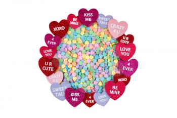 Top view of a circle of hearts, text inside, with a pile of heart shaped candies. Valentines day concept. Isolated on white background. 