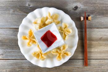 Top view of crispy wanton shells with dipping sauce and chopsticks in holder on rustic wooden boards. 