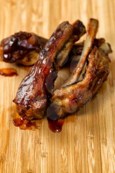 Close up of barbecued ribs with sauce on wooden cutting board. Selective focus on upper front part of ribs in vertical format. 