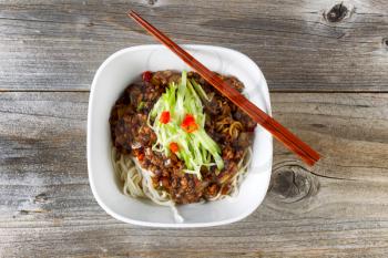 High angled view of noodles with ground beef and cucumbers. Chopsticks on top of bowl with rustic wood underneath. 