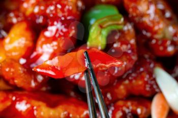 Freshly cooked peppers and chicken in thick sauce. Filled frame format with selective focus on front pepper between chopsticks.  