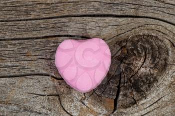 Close up of a single pink heart shaped candy on rustic wood. Valentines day concept. 
