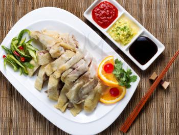 Top view of sliced roasted chicken and vegetables with dipping sauces. Bamboo mat underneath dish. 