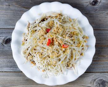 High angled view of Asian dish consisting of noodles, bamboo shoots, peppers and sesame seeds on rustic wood. 