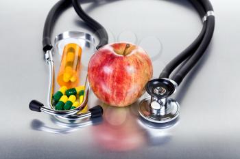 Red apple, medicine capsules and stethoscope on stainless steel table with reflection. Health care concept. 
