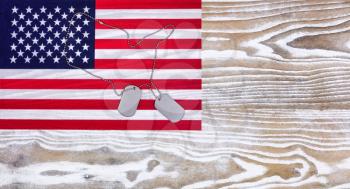 Overhead view of a United of America flag and military ID tags, in outline shape of USA country, on faded white wood. 
