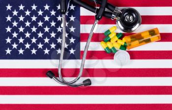 United States of America flag with stethoscope and medication capsules. USA health concept. Overhead view in horizontal layout.