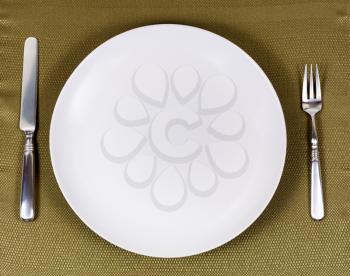 Overhead view of white dinner plate with fork and knife on green table cloth. 