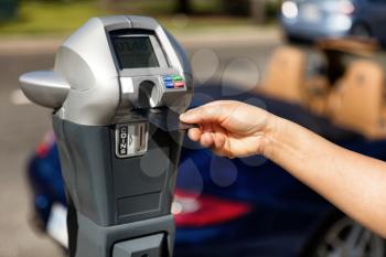 Close up of female hand inserting credit card into parking meter time outdoors on street. Selective focus on hand holding card. 