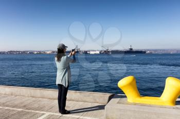 Back view of a woman taking photos with cell phone San Diego bay in Southern California. 