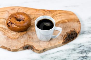 Dark coffee and bagel on wooden server board with marble stone underneath. Selective focus on upper part of coffee cup. 