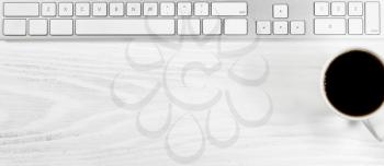 Overhead view of a white desktop with keyboard and coffee. 