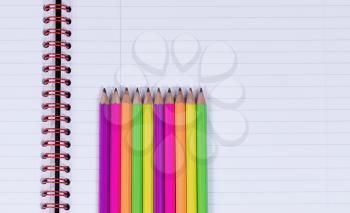 In line colorful pencils, tips facing upward, on a clean spiral notebook. Copy space available. 